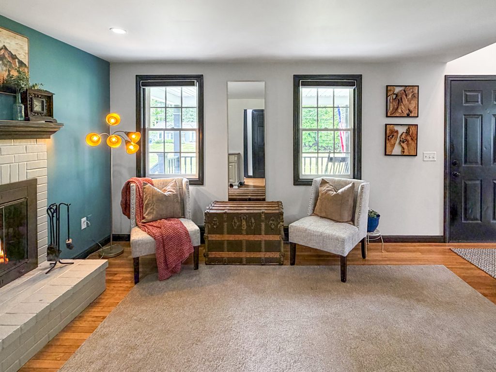 Cozy staged sitting area with fireplace, accent chairs, vintage trunk, warm lighting, and blue feature wall