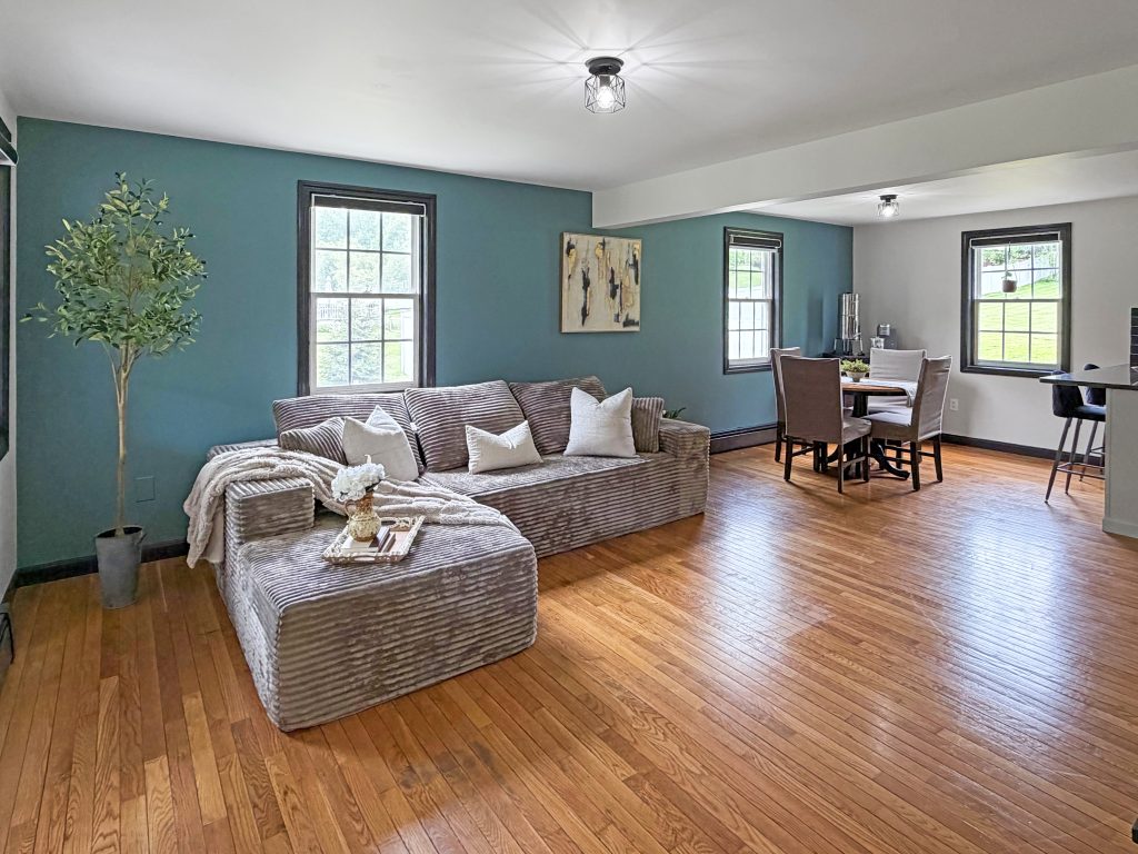 Staged living room with sectional sofa, blue accent wall, hardwood floors, and open dining area