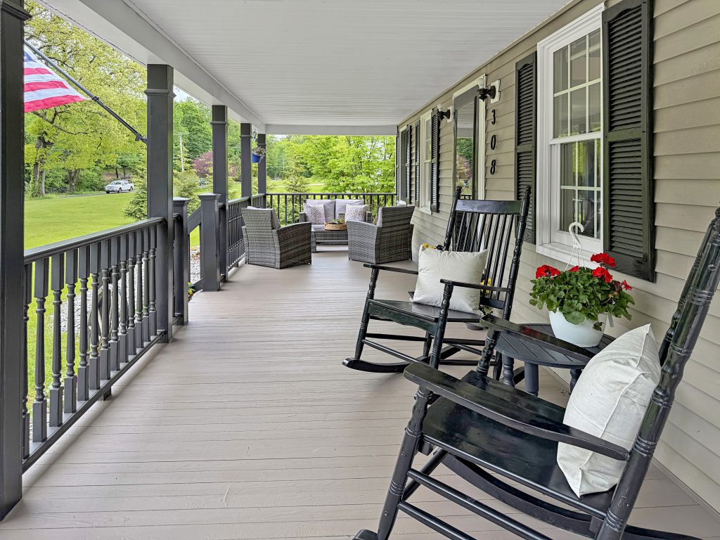 Covered front porch staged with rocking chairs, outdoor seating, and potted flowers overlooking a green yard